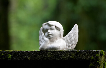 an old, weathered small angel statue with moss in a garden