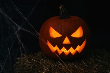 Eerie Halloween pumpkin with illuminated face and spider webs in the shadows