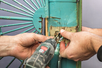 Closeup photo of two male workers installing new lock with drill. Hands installing door lock with...