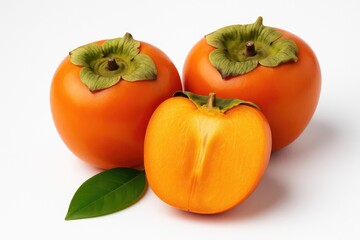 Whole and sliced ripe persimmons with green leaves on a white backdrop