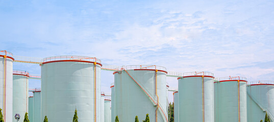 Row of many storage fuel tanks in oil industrial refinery area against blue sky background, Panoramic view with copy space