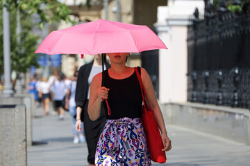 Woman with sun umbrella walk on a street on people background. Hot weather, life in summer city