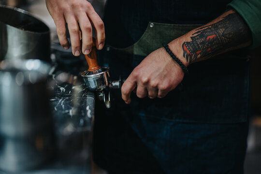 A barista focuses on using a portafilter to tamp coffee grounds while preparing espresso. The scene highlights the art of coffee-making and craftsmanship in a modern cafe environment.