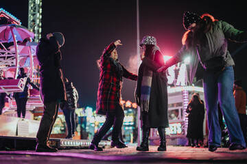 A group of friends gathers at a lively fairground at night, enjoying the vibrant atmosphere. Bright...