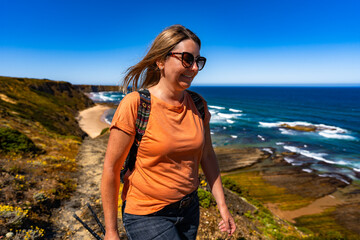Beautiful mid adult woman tourist hiking on trail along Atlantic ocean in nature park Vicentine...