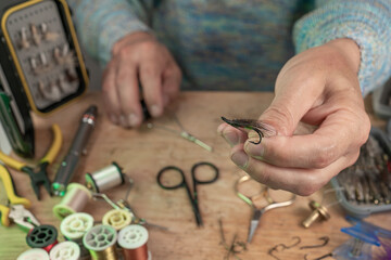 Man making trout flies. Fly tying equipment and material for fly fishing preparation .