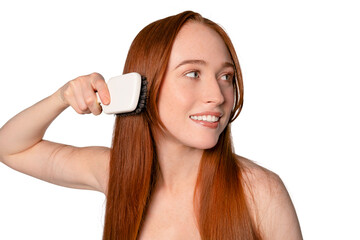 Woman brushes her long red hair with a white hairbrush in a bright, indoor setting showcasing a...