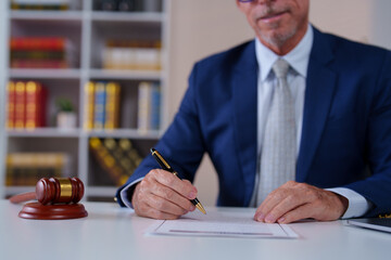 Professional lawyer in a suit meticulously reviewing a legal document at a desk. A gavel sits...