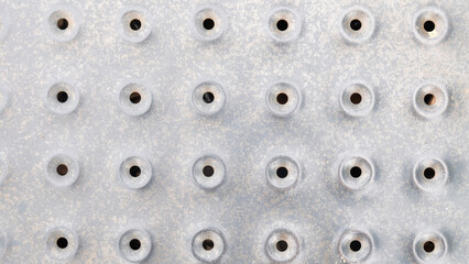 A silver metal surface with a pattern of small, evenly spaced circular indentations, each with a...