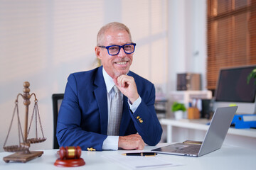 Professional lawyer in a suit working at a desk with a laptop, legal scales, and a gavel. The office setting is bright and organized, reflecting a modern legal environment
