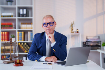 Senior lawyer sitting confidently at his desk, resting his chin on his hand, surrounded by a laptop...