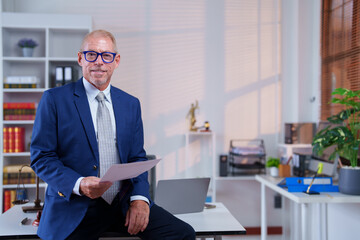 Portrait of a confident and successful mature lawyer holding legal documents and sitting on his...