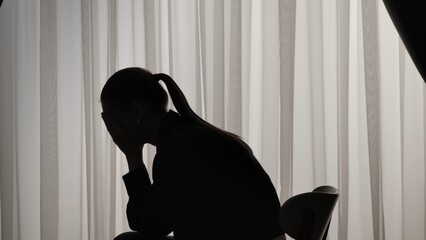 Silhouette of a distressed woman in front of backlit curtains
