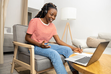 Young woman in headphones sitting at laptop and looking busy