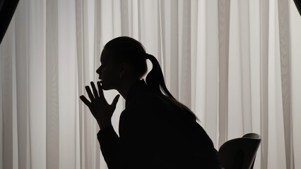 Silhouette of a distressed woman in front of backlit curtains