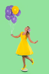 Cheerful woman in yellow dress holds purple balloons against a bright green background, capturing a playful moment of joy and celebration