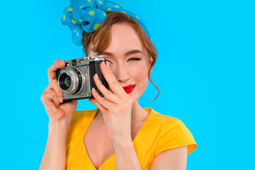Woman in yellow dress smiles while taking a picture with vintage camera against bright blue...