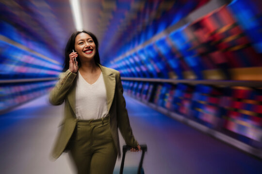 Confident businesswoman talking on phone while walking with luggage in a dynamic urban setting