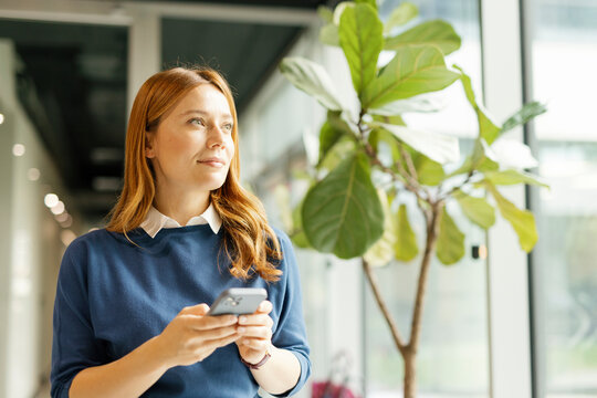 Woman in office holding smartphone and looking inspired