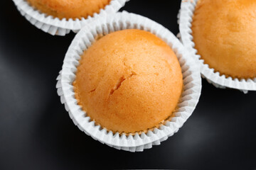 Fresh baked vanilla cupcakes in paper cups on black ceramic plate. Fluffy sweet muffins. Top view. 