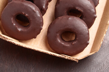 Chocolate donuts in cardboard pack on wooden table. Sweet baked dessert doughnuts. Close up. 
