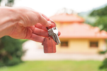 Hand of property owner holding a door keys bunch against country house background in ecological...
