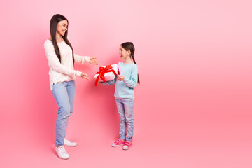Young girl gives a present to her smiling mother in front of a pink background, showcasing love and...
