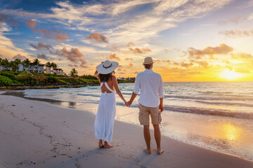 A romantic couple stands of a tropical beach holding hands and enjoys the beautiful sunrise or sunset