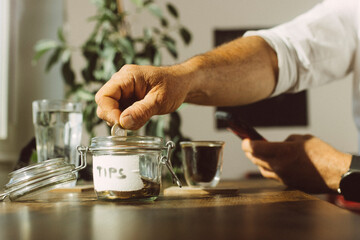 Businessman putting tip in jar on table at coffee shop