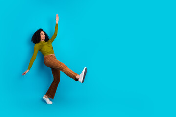Joyful young woman strikes a playful pose against a vibrant blue background showcasing casual and...