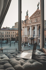 Cozy workspace with an open laptop by a window overlooking the historic Lviv Opera House and...