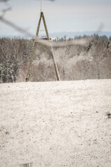 Snow covered agricultural hill field with a triangle wood tower on top on a bright winter day