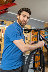 Handsome mechanic adjusting bike wheel in workshop for tire repair
