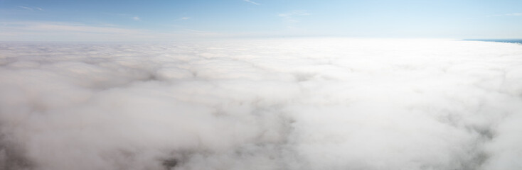 A high altitude perspective showing a vast layer of white clouds blending with the horizon, set beneath a clear blue sky with no visible landmarks.