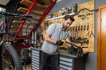 Velomechanic in professional attire servicing bicycle with specialized tools in workshop setting