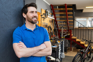Man mechanic posing in bike shop door wearing blue t-shirt