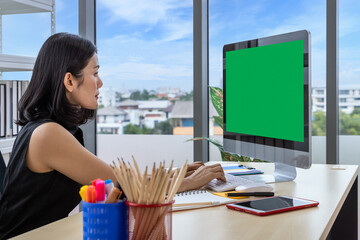 Asian businesswoman female typing at office desk using desktop computer with green screen