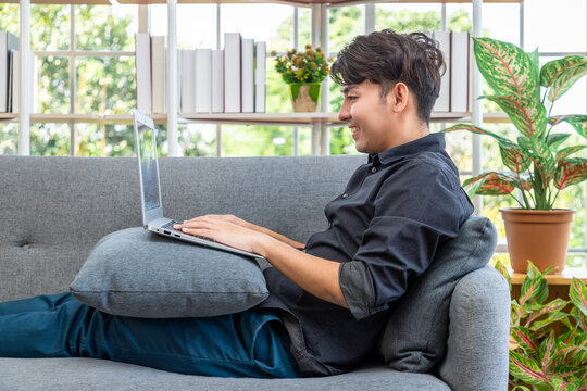 Young Asian man working using laptop on sofa home casual comfortable lifestyle indoors