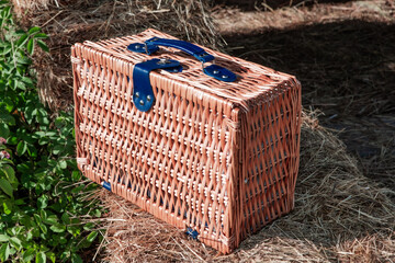Beautiful picnic suitcase made of woven straw stands in haystacks. Organic handmade products.