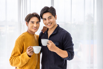 Asian LGBT gay couple smiling and enjoying morning coffee together at home, looking at camera