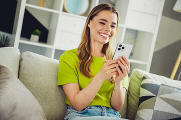 Joyful young woman using her smartphone while relaxing on the sofa at home in a cozy living room area