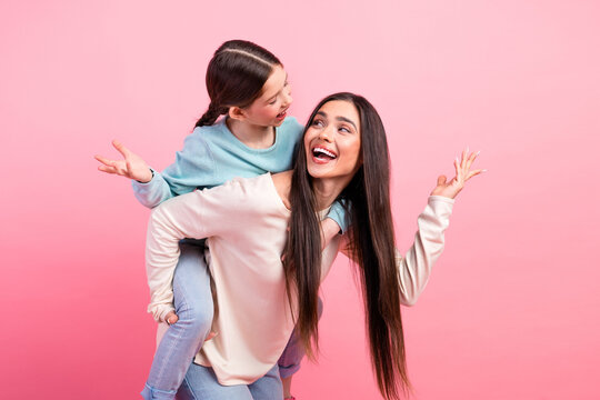 Mother and daughter posing joyfully together against vibrant pink background, radiating happiness, love, and shared moments