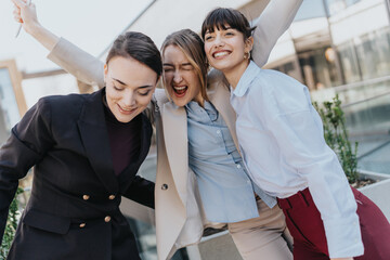 Obraz premium A happy trio of young professional women expressing joy and camaraderie in an outdoor modern setting. A moment capturing success and teamwork in a professional and urban background.