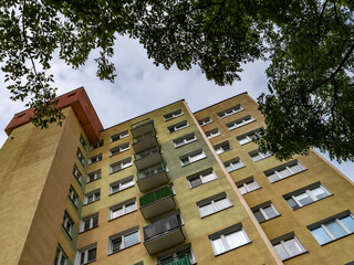 Low-angle view of an old apartment block with balconies, framed by tree branches. Urban housing in Eastern Europe with a nostalgic, utilitarian feel