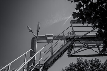 Industrial staircase leads to the sky above a tree line on a bright day, showcasing a blend of...