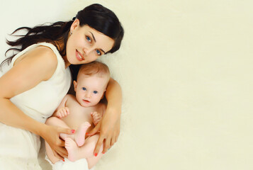 Portrait of happy young mother lying with sleepy baby together on bed at home