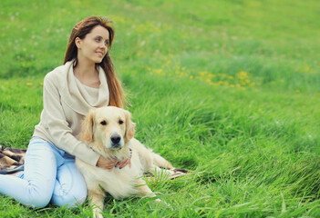 Happy owner young woman with Golden Retriever dog sitting on grass together in summer park