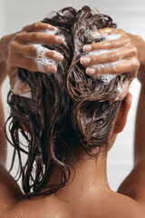 Naklejka premium A beautiful woman washing her long hair in shower with shampoo foam and water. Self-care and hygiene concept for health.