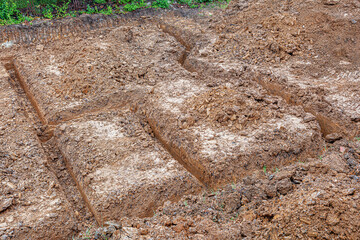 Brown earth with dug trenches for a construction foundation, viewed from above.