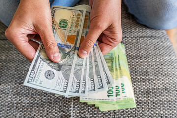 A person sitting indoors in jeans while holding and comparing euro and dollar banknotes,...